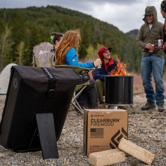 PACKFIRE travel backpack and two ClearBurn Firewood bricks with their box, in front of friends around the PACKFIRE fire pit by a mountain lake