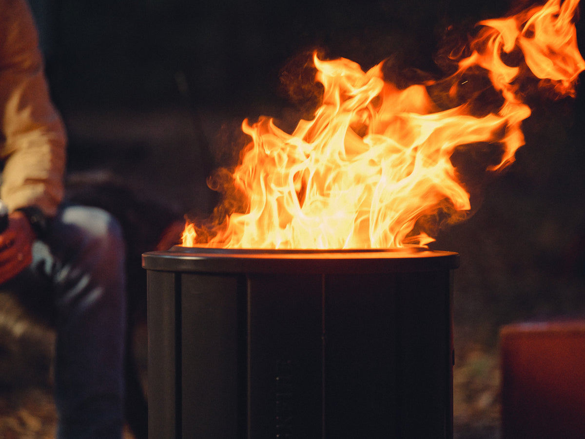 Person wearing gloves sitting next to a fire pit with flames