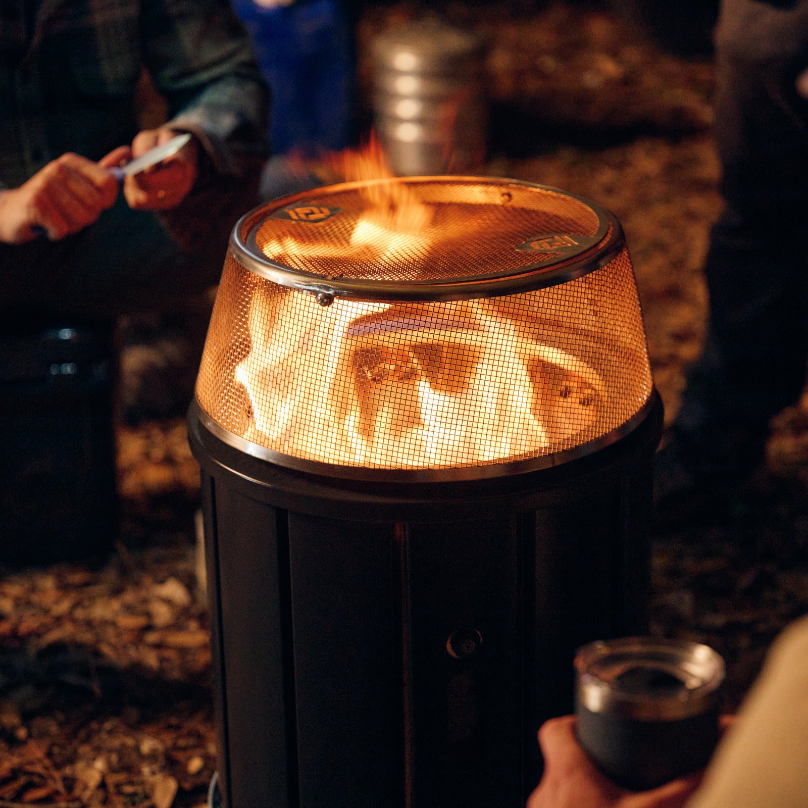 Glowing orange flame inside metal mesh fire pit top with black outer housing